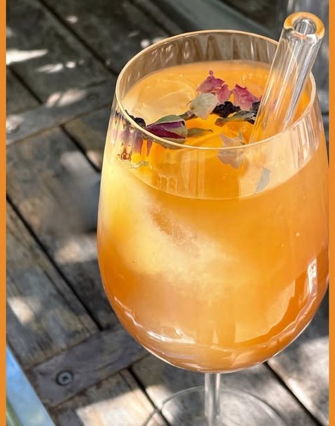Un grand verre de boisson fraîche orangée, pétales de fleurs et paille en verre
