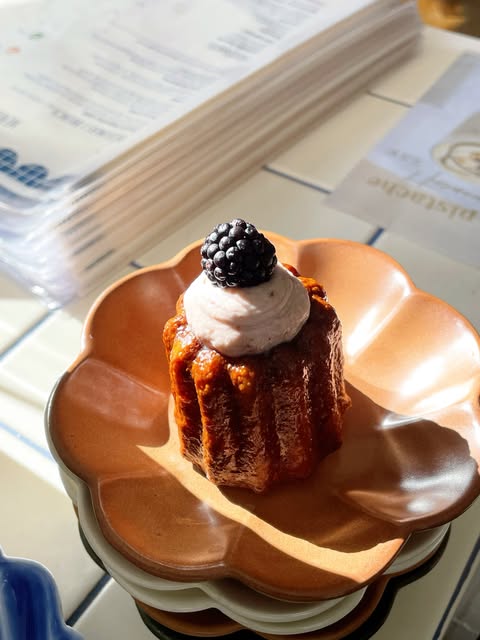 Un cannelé fourré, surmonté d’une mûre, sur une assiette terracotta en forme de fleur