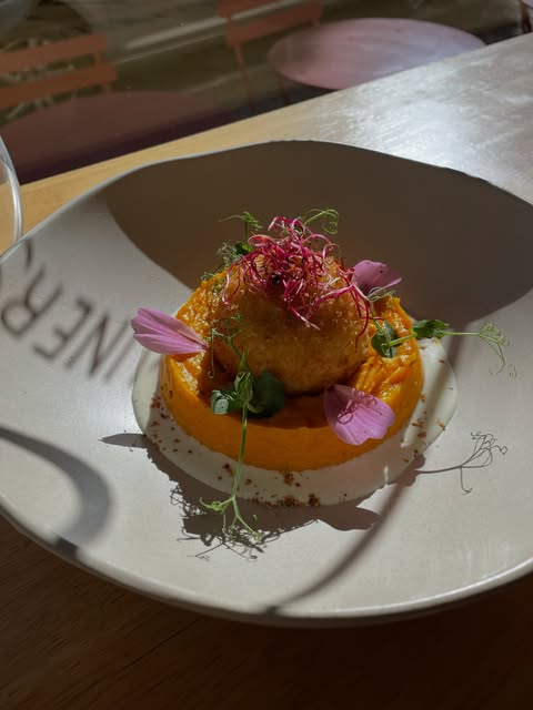 Un cromesquis doré posé sur une purée de potimarron, fleurs et jeunes pousses