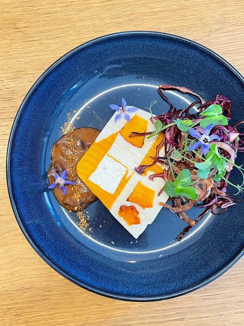 Une assiette bleue : tofu mariné, courge, jeunes pousses et fleurs