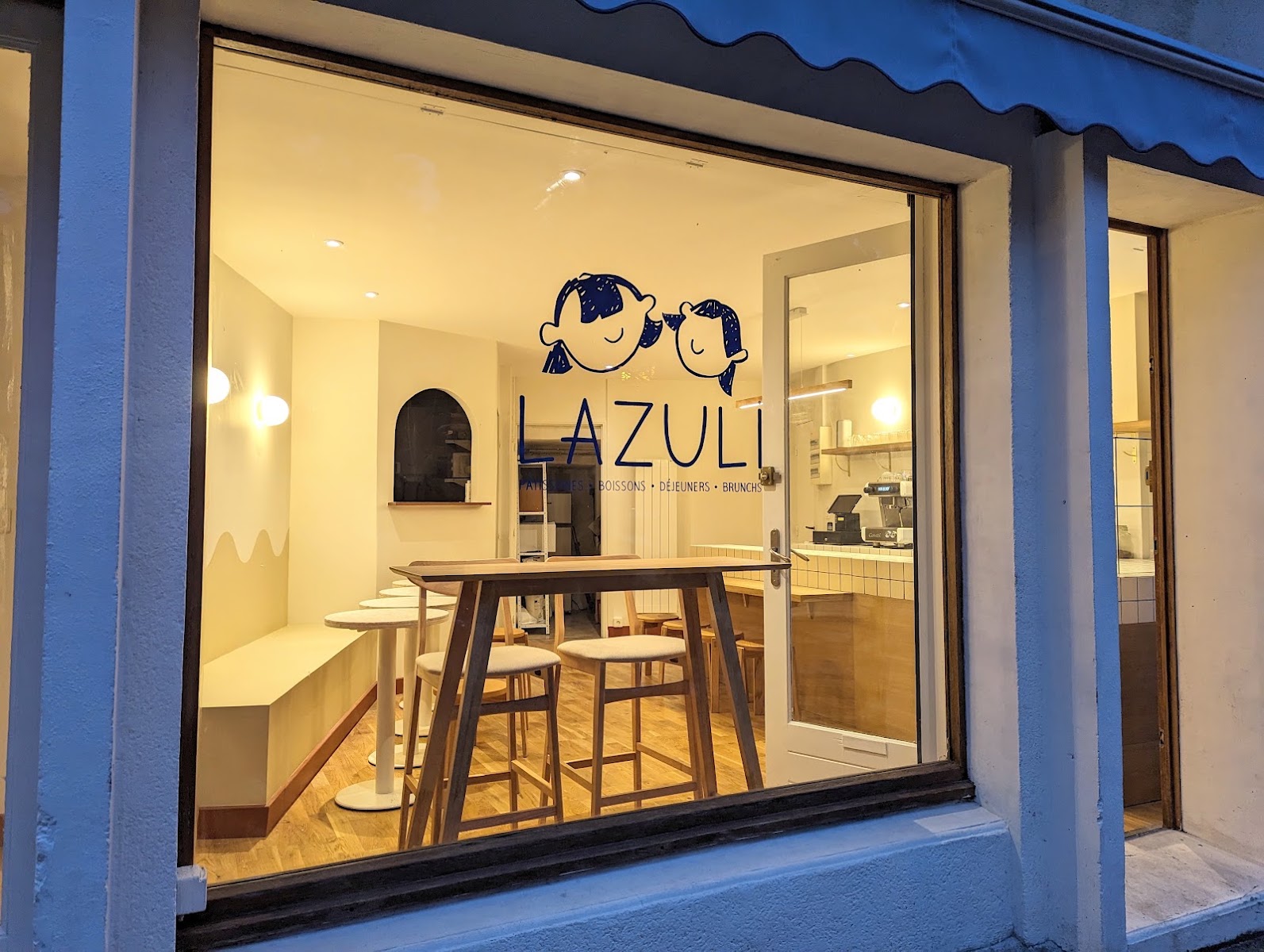 La salle LAZULI vue de la rue, tables hautes en bois clair et logo bleu sur la vitrine