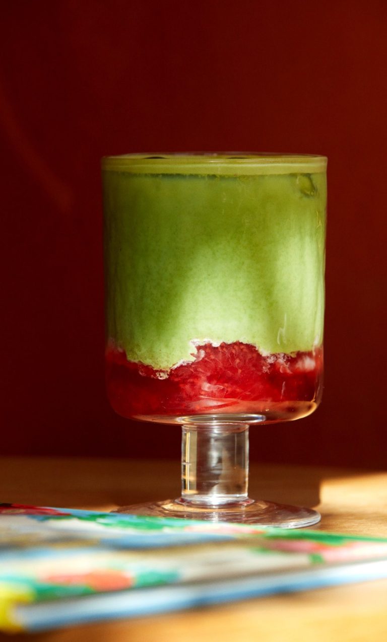 Un verre de matcha latté sur un coulis de fraise, dans la lumière du matin