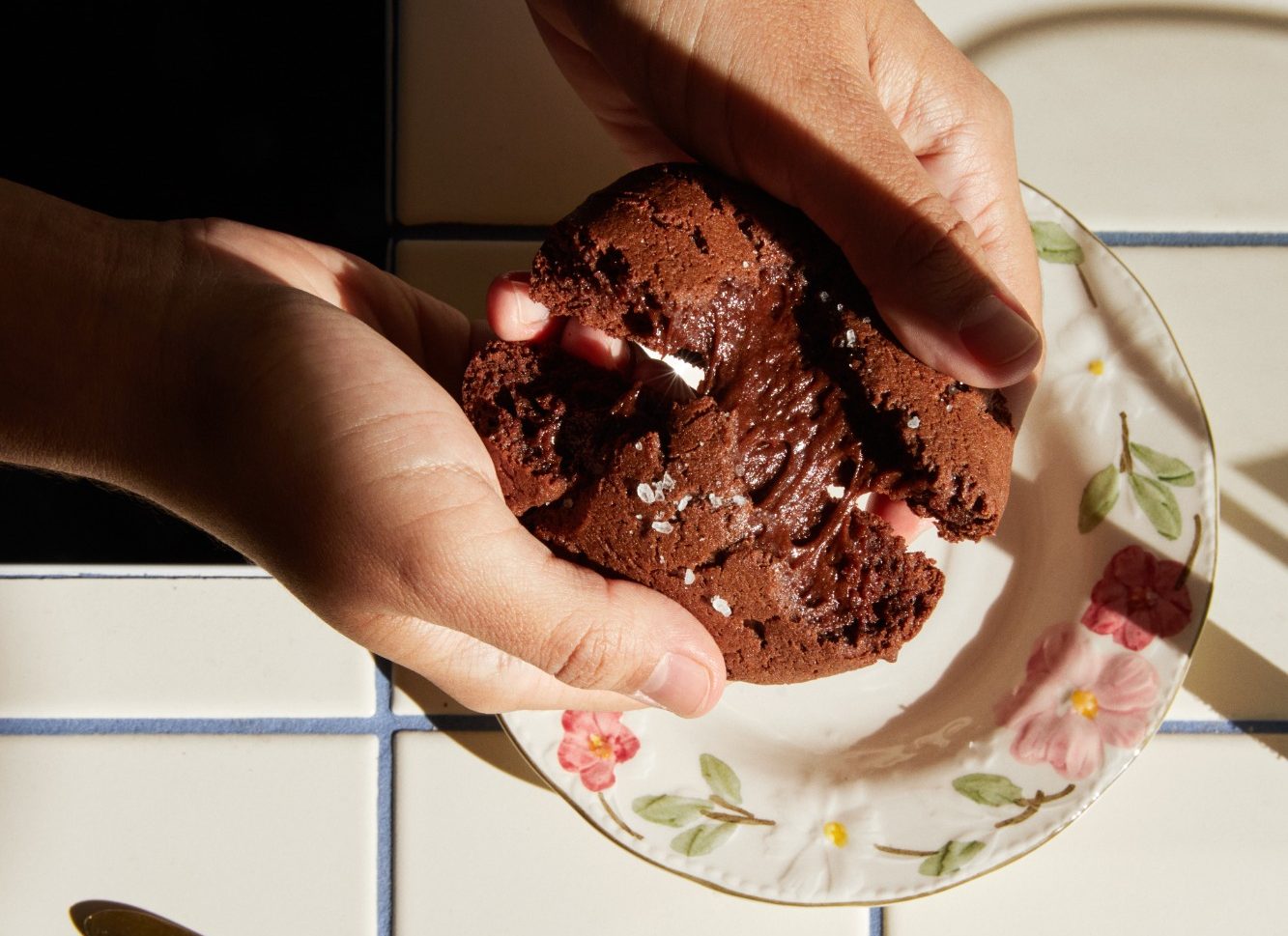 Un cookie au chocolat que l’on casse en deux, cœur coulant, posé sur une assiette fleurie