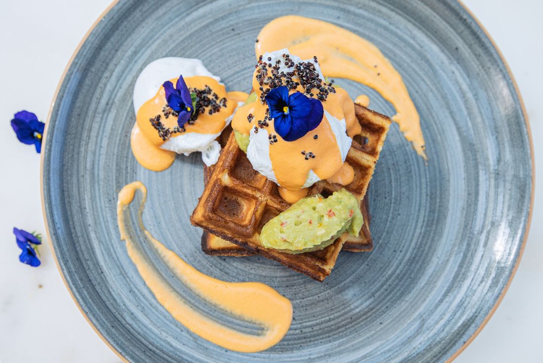 Gaufre salée, œuf poché et fleurs comestibles dans une assiette bleue (photo d’illustration)